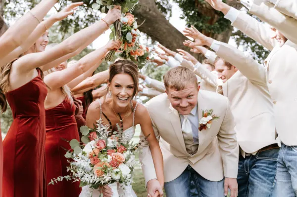 Bride and groom walking through a cheering wedding party arch outdoors