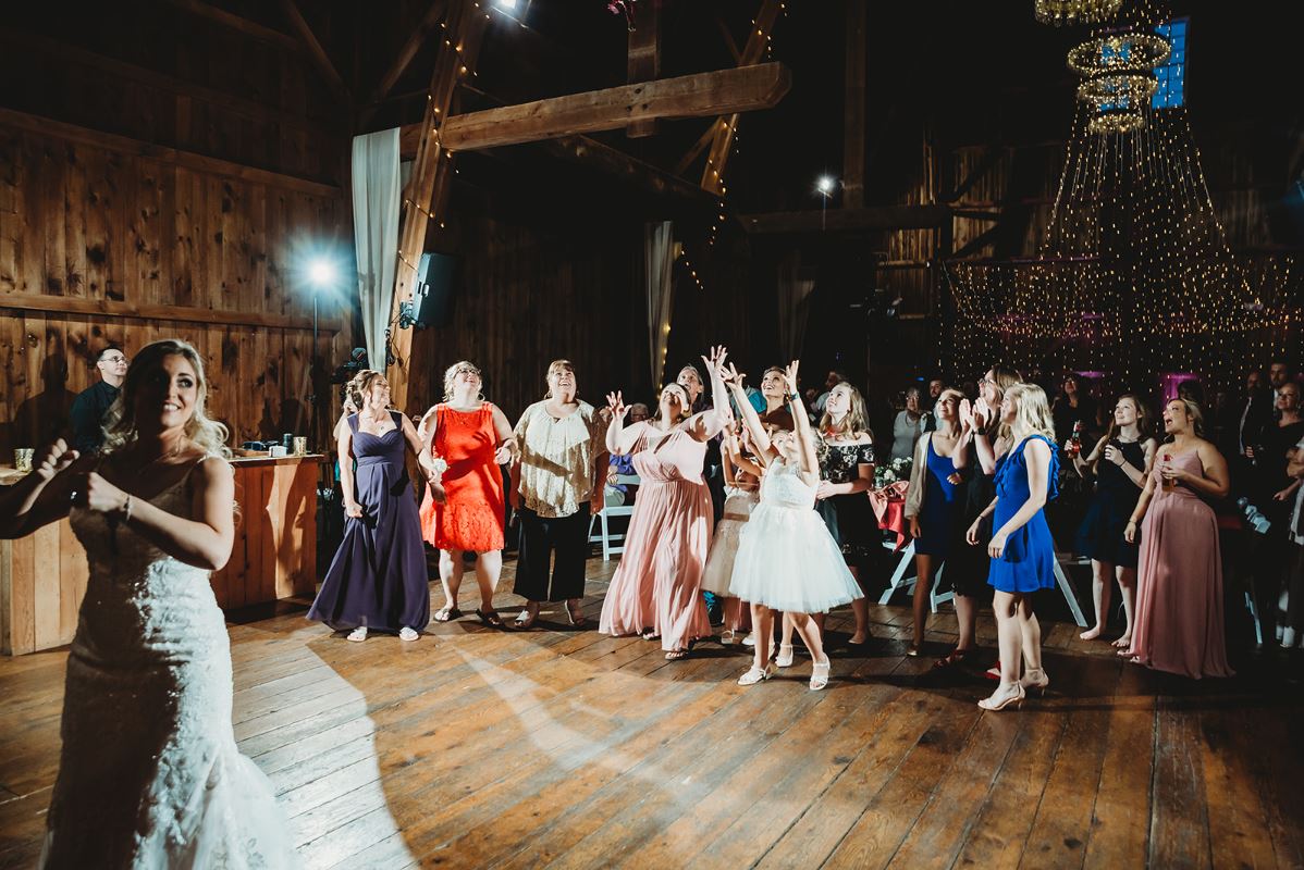Bride tossing bouquet to cheering guests in a barn reception