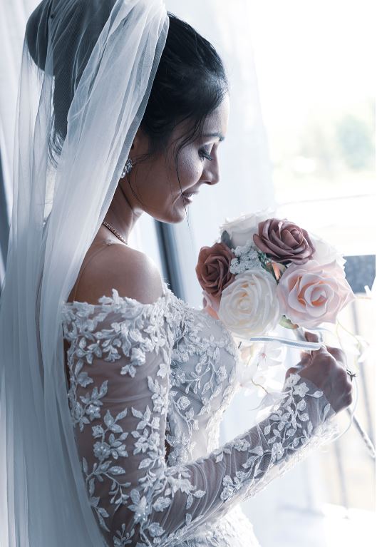 Bride in lace gown holding bouquet by soft window light
