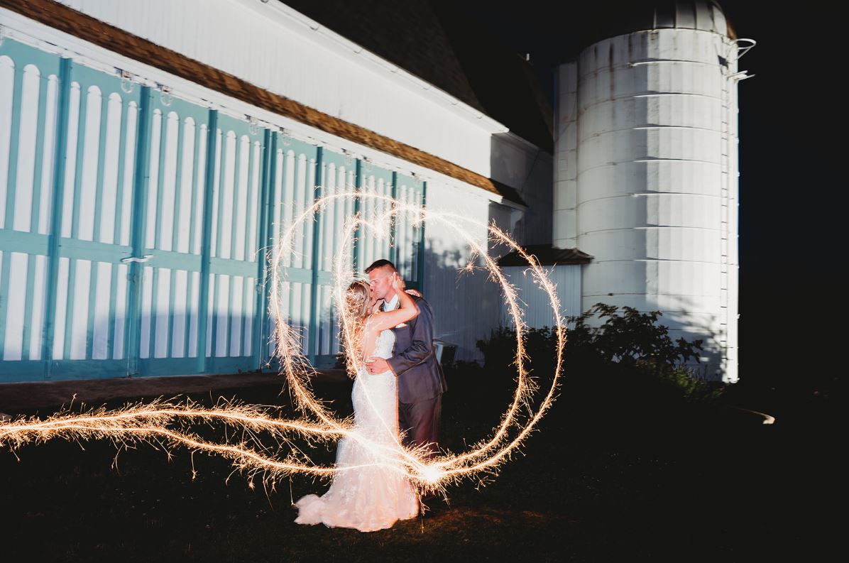 Bride and groom kissing inside a heart of sparkler light at a barn wedding